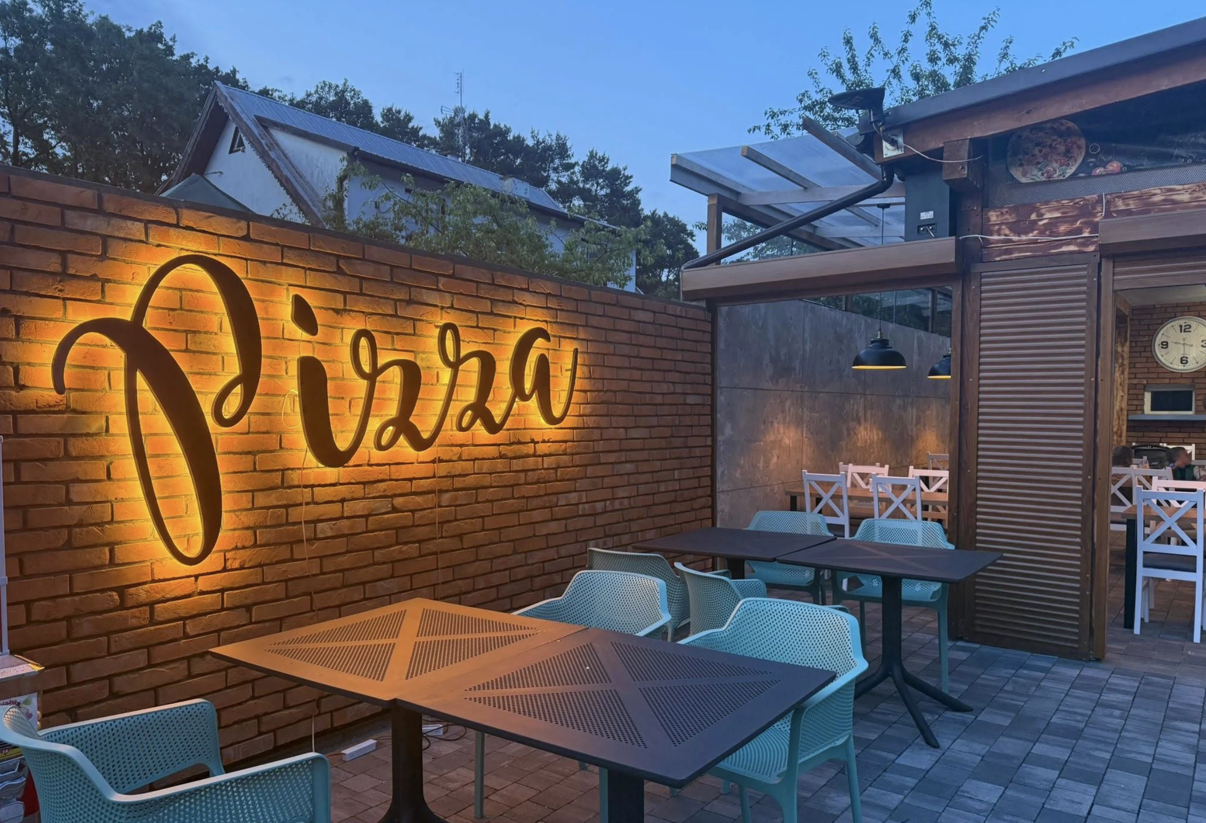 Klimatyczny ogródek Forno Vivo we Wrocławiu z podświetlanym napisem Pizza o zmierzchu