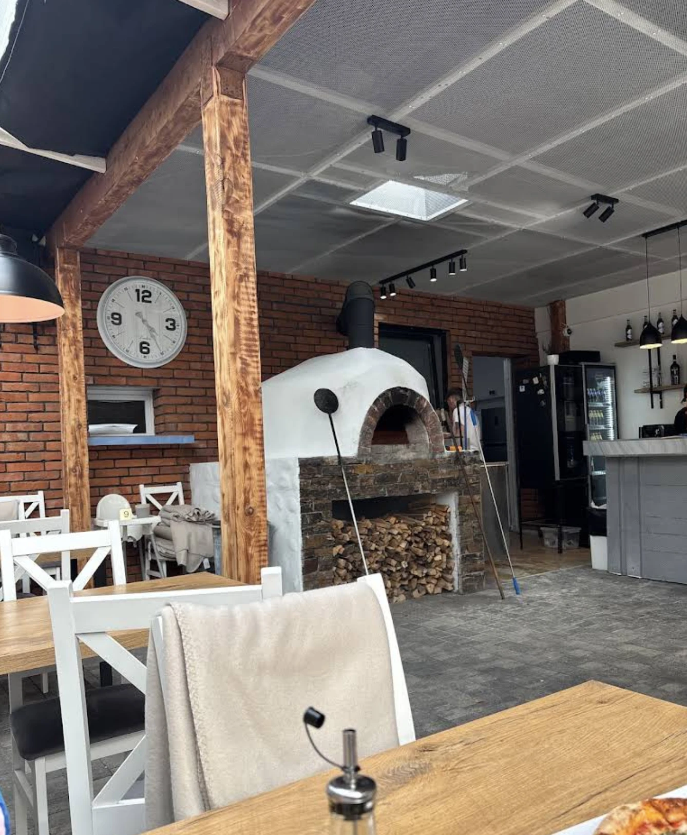 Piec opalany drewnem na środku lokalu Forno Vivo we Wrocławiu, ceglana ściana i drewniane stoły